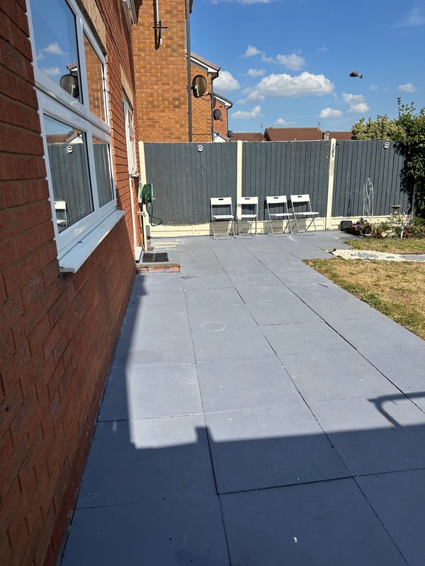Paved patio area beside brick house with metal fencing and garden beyond