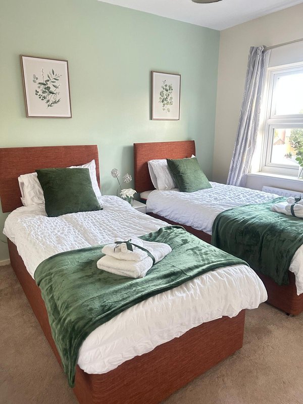 Twin bedroom with two beds, green accents, framed botanical prints and window with curtains