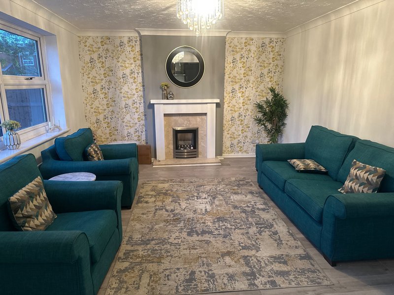 Living room with teal sofas, fireplace with mirror, patterned wallpaper and rug
