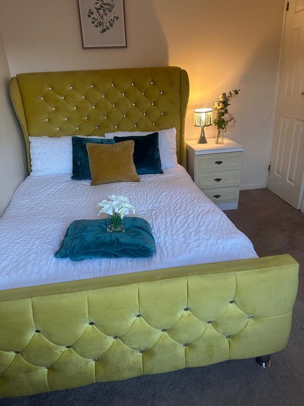 Bedroom with olive-green upholstered bed, white bedding, decorative pillows, and wooden nightstand