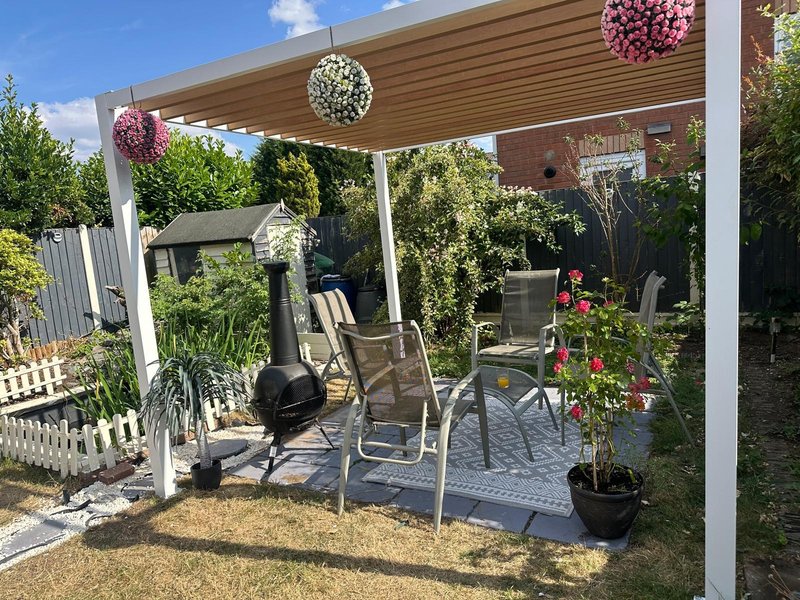 Garden patio with pergola, outdoor seating, hanging flower baskets, and landscaping