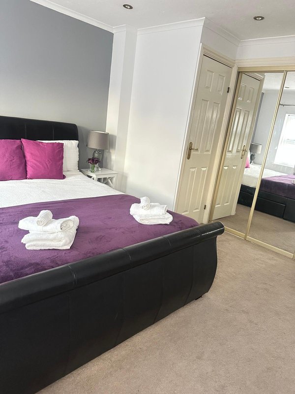 Modern bedroom with purple bedding, black bed frame, pink cushions and white towels