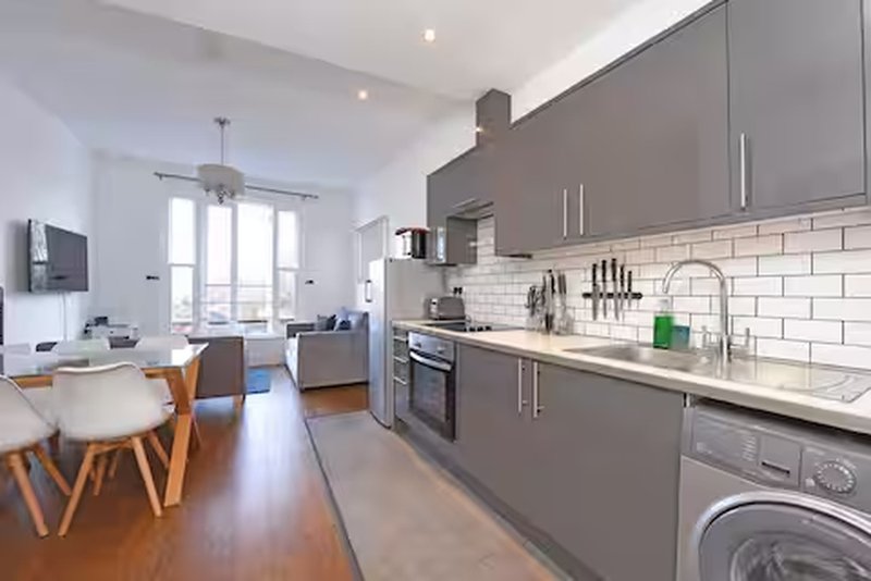 Modern open-plan kitchen and dining area with gray cabinetry, white subway tiles, and wooden flooring