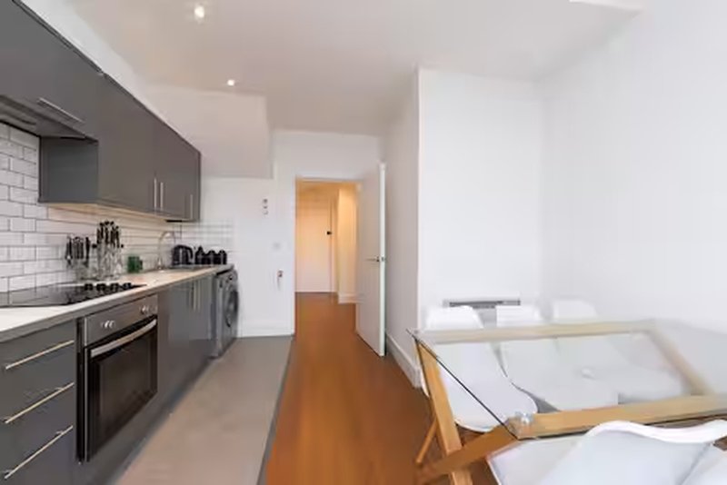 Modern kitchen with grey cabinets, white subway tile backsplash, and wooden flooring extending into living area