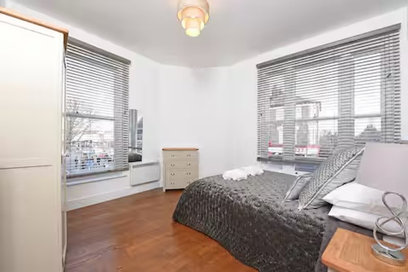 Bright bedroom with double bed, wooden floor, desk by windows, and city views