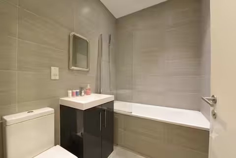 Modern bathroom with white toilet, black vanity, mirror, and bathtub with grey tile walls