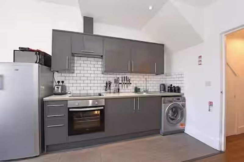 Modern kitchen with dark grey cabinets, white subway tile splashback, integrated appliances and wooden floor