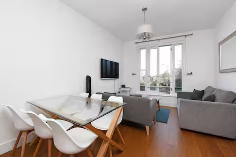Modern open-plan living room with dining table, grey sofa, wall-mounted TV and glass doors to balcony