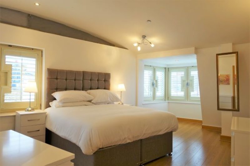 Spacious bedroom with queen bed, upholstered headboard, windows and wooden flooring