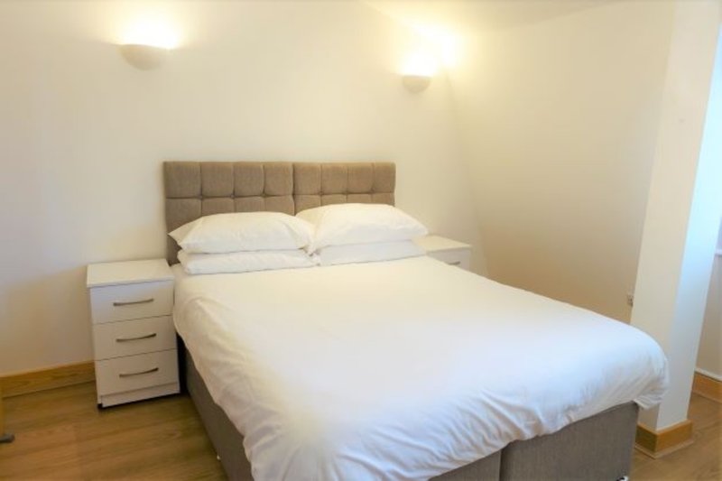 Modern bedroom with queen bed, upholstered headboard, white bedding and wooden flooring