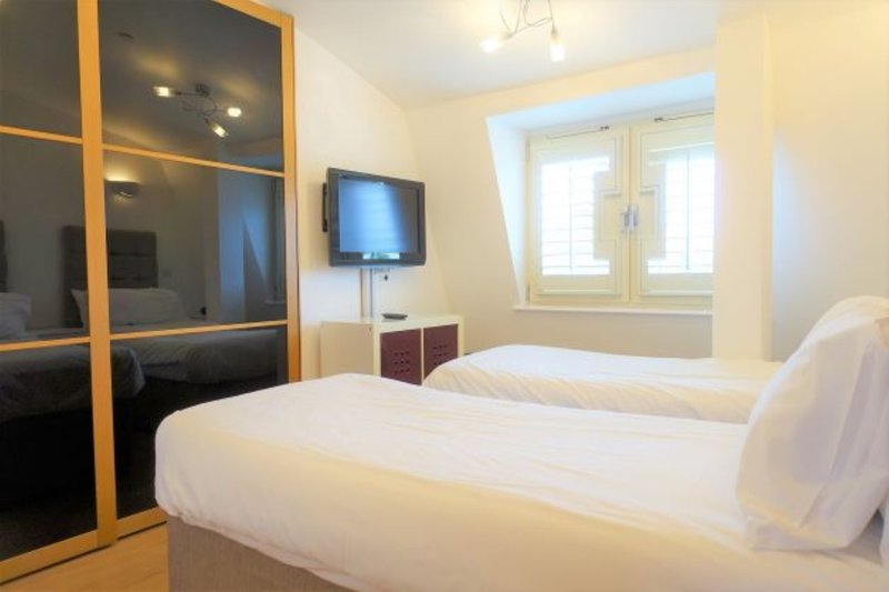 Bright bedroom with two single beds, wooden wardrobe, wall-mounted TV and window