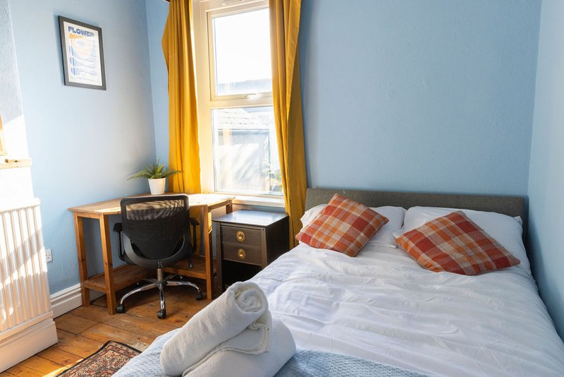 Bright bedroom with double bed, wooden desk, chair, and yellow curtains by window