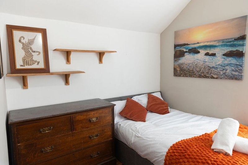 Bedroom with double bed, wooden dresser, framed artwork, floating shelves and beach photograph