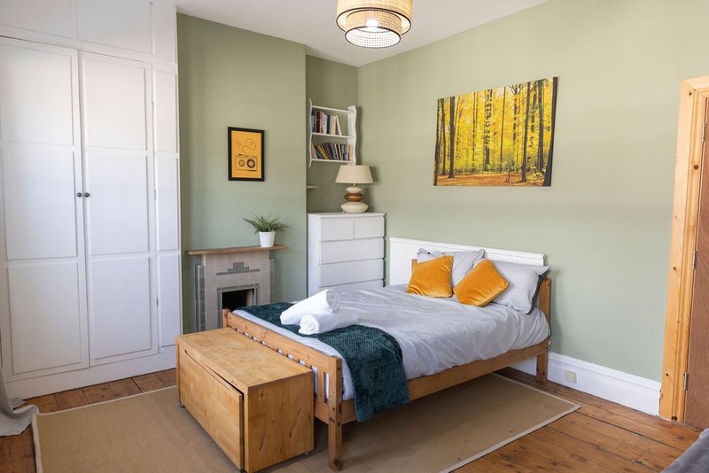 Bedroom with wooden bed, white wardrobe, green walls, wall art and soft furnishings