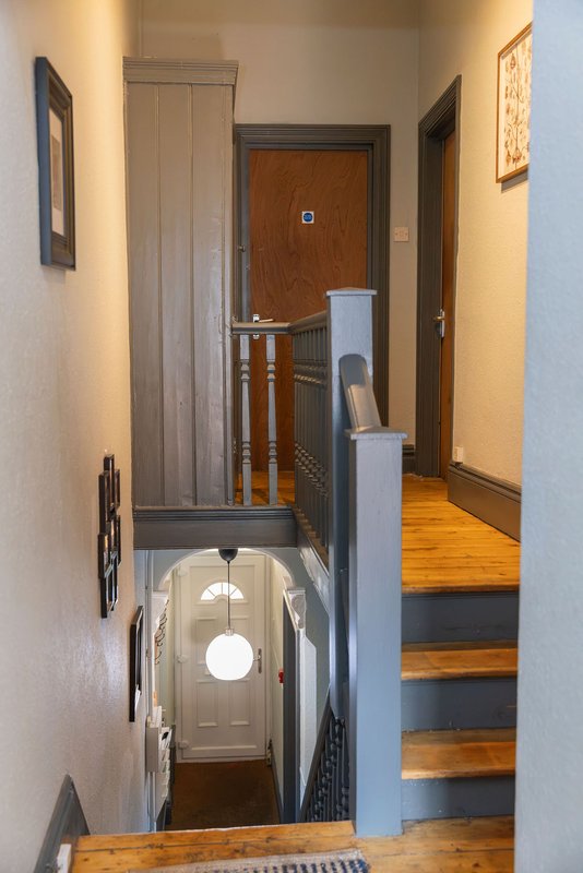 Hallway and staircase with wooden steps, cream walls, and brown doors leading to upper level
