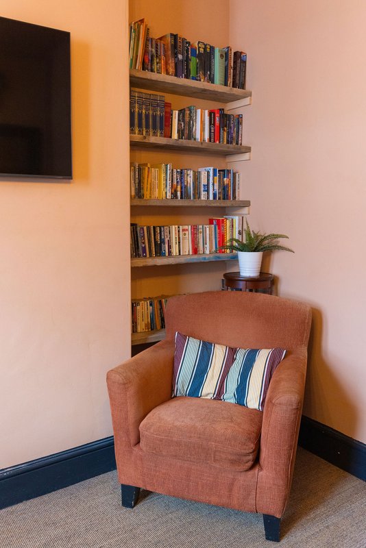 Cozy reading nook with terracotta armchair, striped cushion, wall-mounted bookshelves, and potted plant