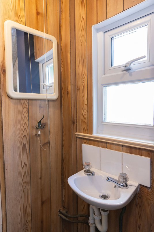Small bathroom with wooden walls, wall-mounted sink, mirror, and window