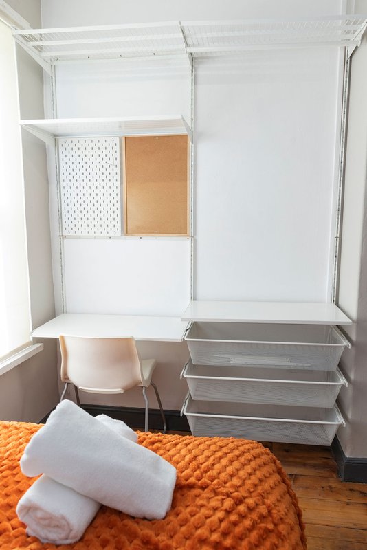 Bedroom wardrobe interior with white shelving, storage boxes, chair and rolled towels