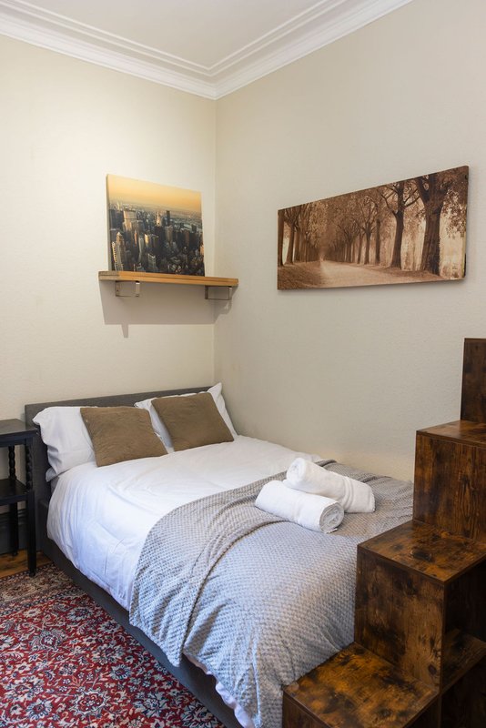 Bedroom with double bed, white bedding, wooden furniture, framed wall art and shelf decoration