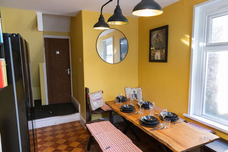 Bright yellow kitchen-diner with wooden table, black pendant lights, and modern furnishings