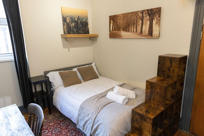 Bedroom with double bed, white bedding, wooden storage steps, wall art and grey curtains