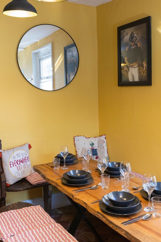 Bright yellow dining room with wooden table, black plates, glasses, and framed artwork on wall