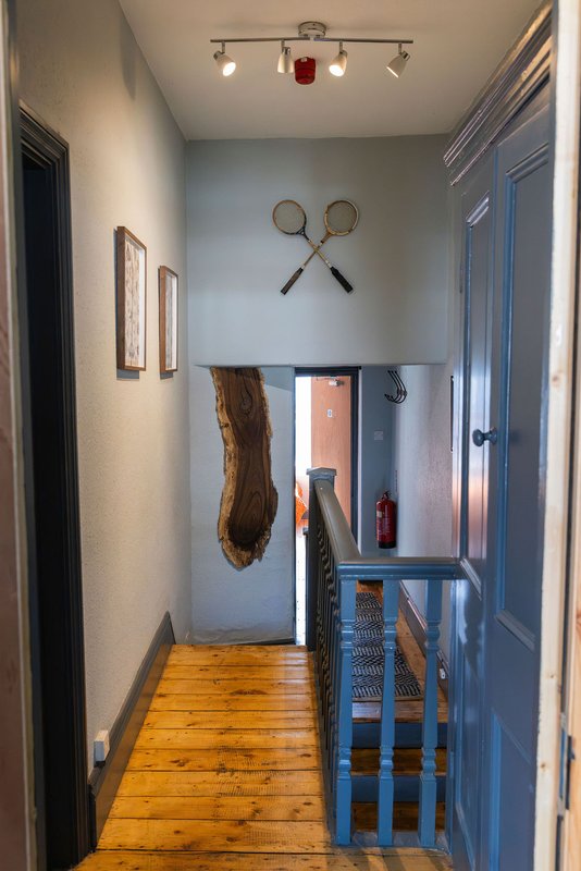 Narrow hallway with wooden floor, blue doors, and decorative wall items including crossed rackets and driftwood