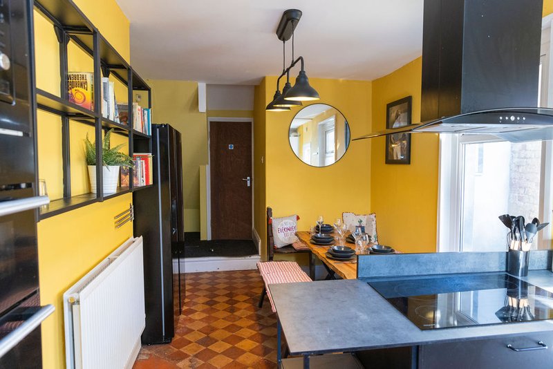 Modern kitchen with yellow walls, black cabinetry, blue island, and open-plan dining area