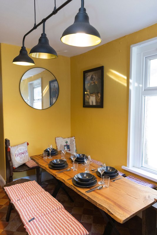 Bright yellow dining room with wooden table, black pendant lights and round mirror