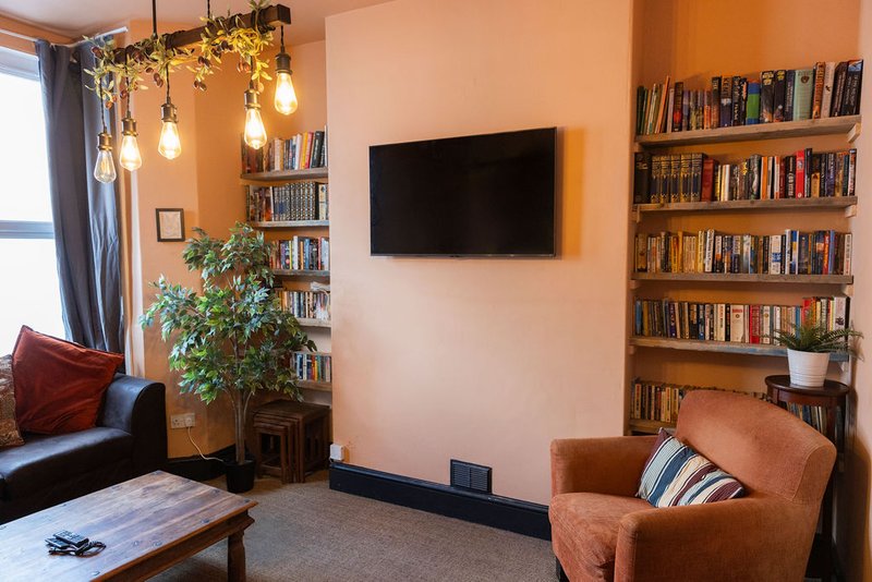 Warm living room with bookshelves, wall-mounted TV, pendant lighting, and upholstered seating