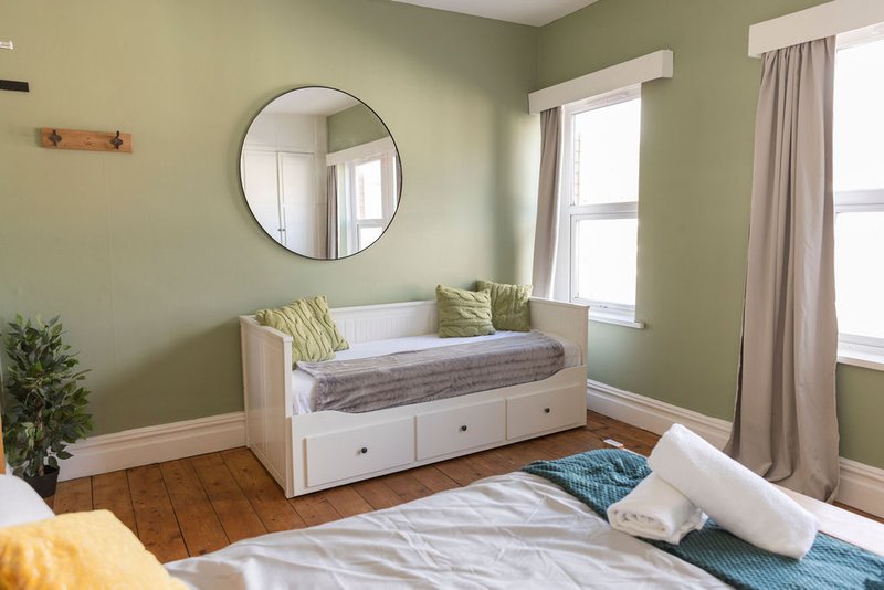Bedroom with green walls, white daybed with storage, round mirror, and hardwood flooring