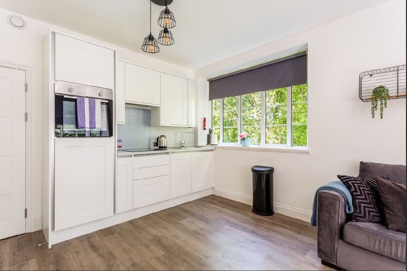 Open-plan kitchen and living area with white cabinetry, wooden flooring, and seating area