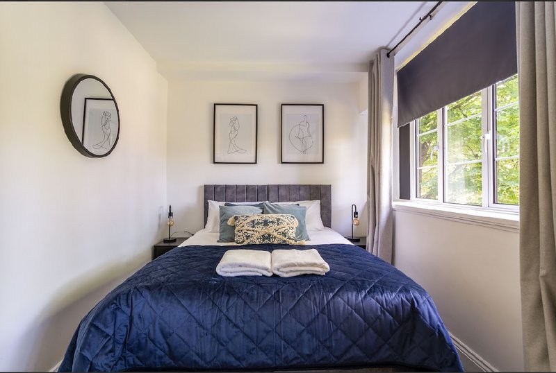 Modern bedroom with navy quilted bed, framed wall art, round mirror, and large windows