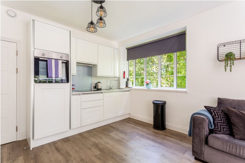 Modern kitchen with white cabinetry, built-in appliances, pendant lighting, and adjacent seating area.