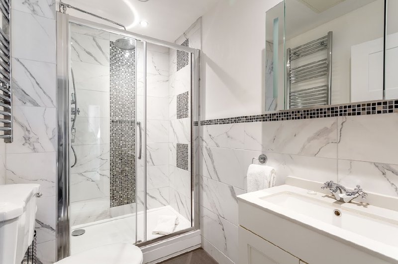 Modern bathroom with marble tiles, shower enclosure, vanity sink and mirror