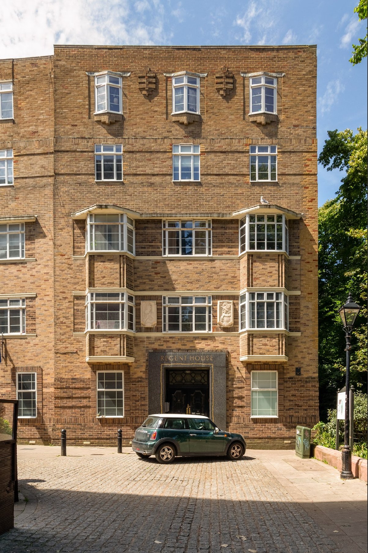 Brick residential building with multiple windows and parked car in front courtyard