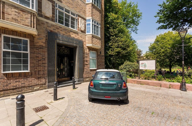 Brick building exterior with parked car, entrance door, bollards and surrounding trees