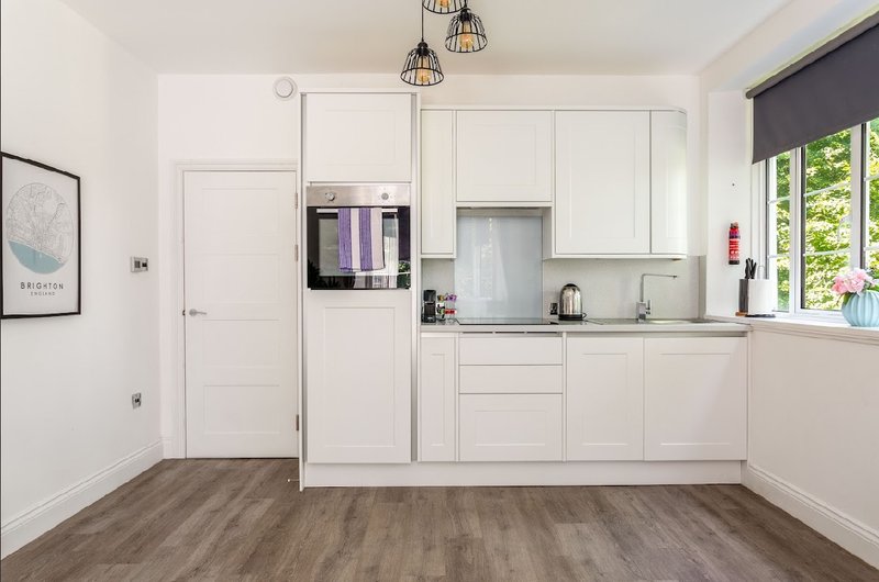 Modern white kitchen with built-in appliances, wooden flooring, pendant lights and garden view