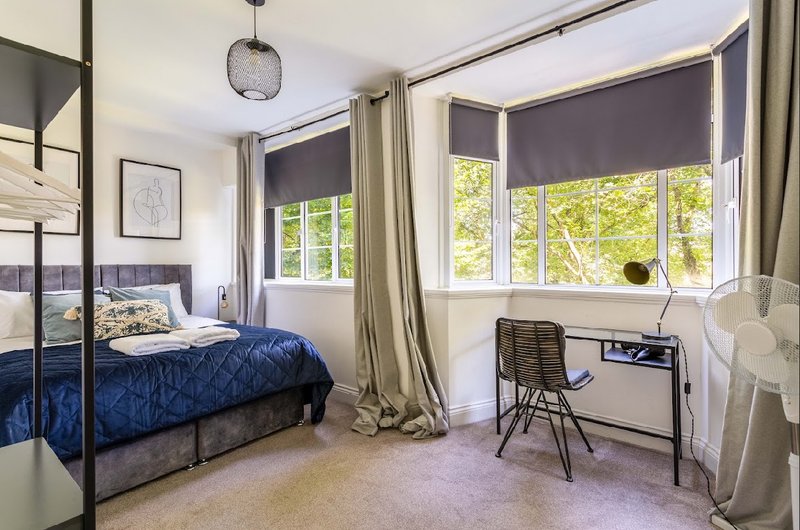 Bright bedroom with four-poster bed, desk, chair, and large windows with views
