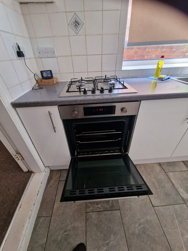 Kitchen counter with gas hob, oven, white cabinetry and yellow cleaning bottle