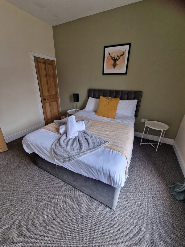 Bedroom with double bed, white bedding, yellow cushion, framed deer artwork, wooden door.
