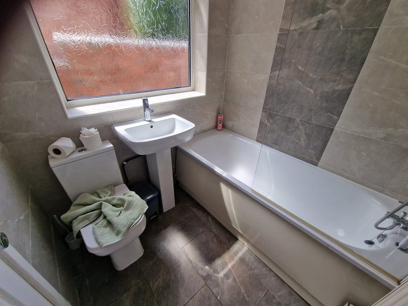 Modern bathroom with bathtub, pedestal sink, toilet, window and grey tile walls