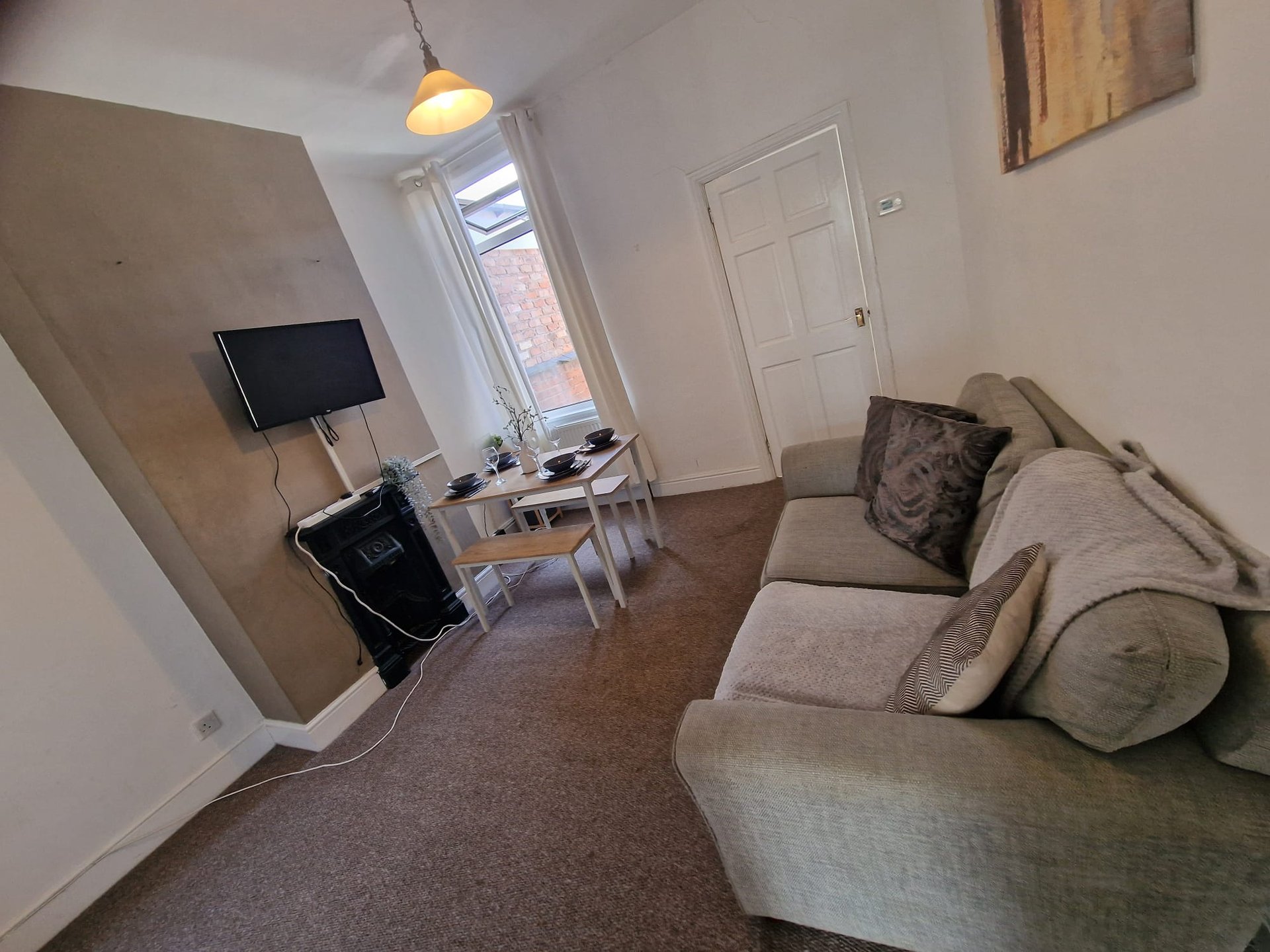 Living room with beige sofa, TV on stand, desk, pendant light and window