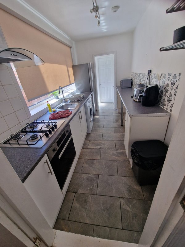 Galley kitchen with white cabinetry, gas stove, oven, and countertop appliances