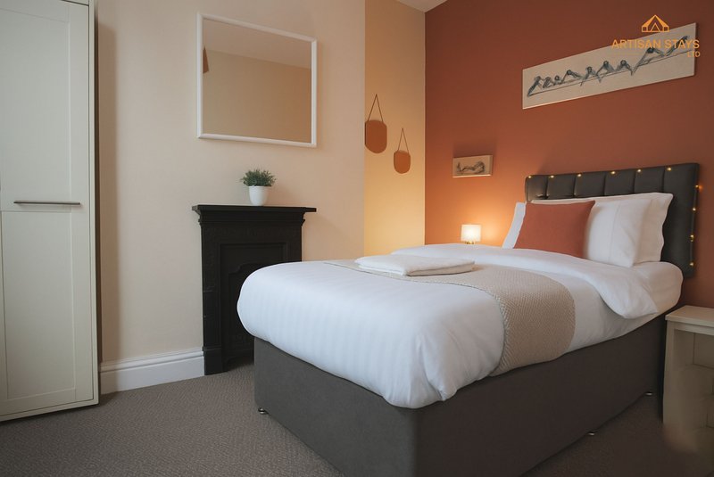 Modern bedroom with double bed, orange accent wall, fireplace, and pendant lighting