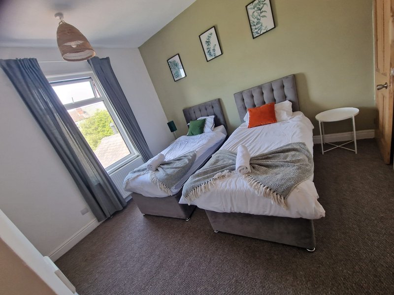 Bedroom with two single beds, gray headboards, white bedding, window with blue curtains, wall art