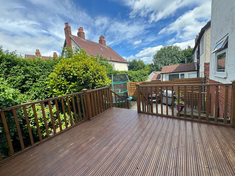 Wooden deck with brown railings overlooking garden and neighboring houses
