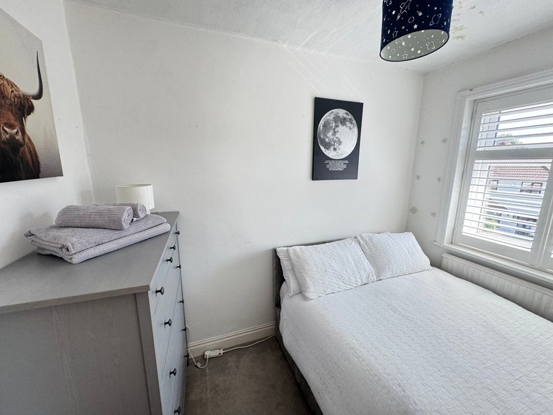 Small bedroom with white bed, dresser, moon poster and shuttered window