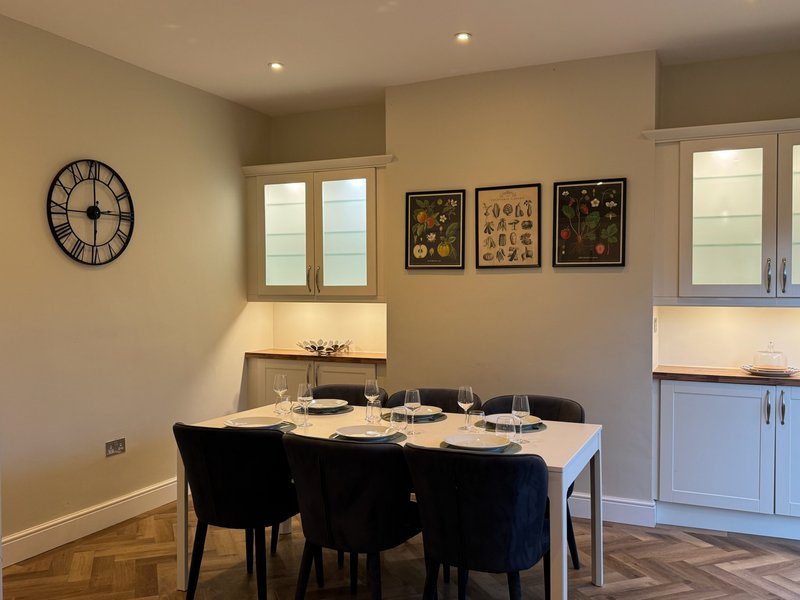 Dining room with set table, black chairs, wall clock and framed botanical prints