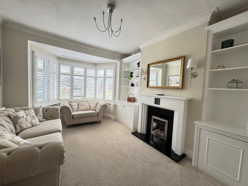 Bright living room with cream sofa, bay window with shutters, fireplace and built-in shelving